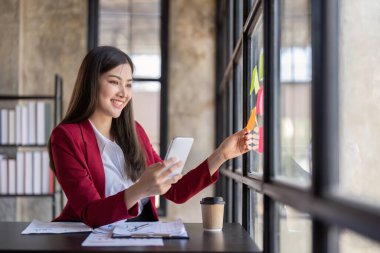 businesswoman talking on cellphone, writing notes on colorful papers in office, employee checking financial documents, working with statistics, consulting client by phone call.