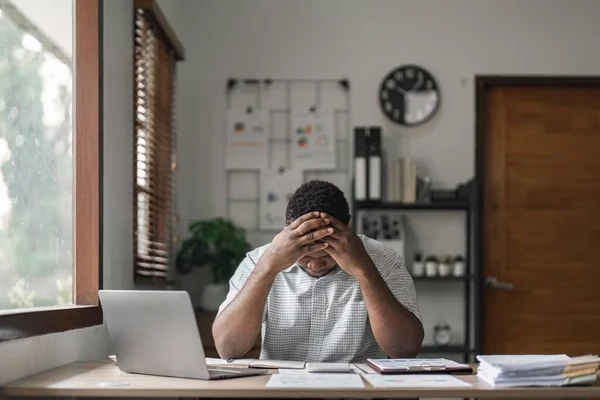 Tired depressed african businessman frustrated by business failure bankruptcy looking at laptop feel exhausted having headache, upset stressed black office worker worried about problem at work.