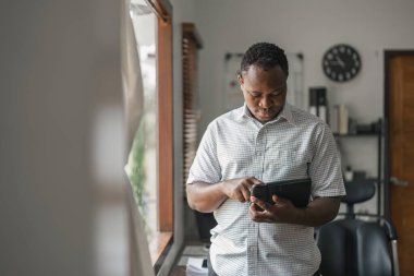 Gülümseyen Afrikalı Amerikalı serbest yazar evdeki yeni projede çalışırken ekran dijital tabletine dokunuyor. İnternet 'te bilgi arayan siyah işadamı.