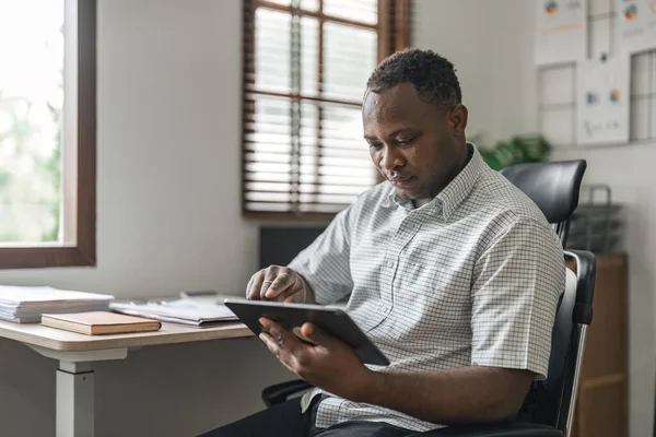 Smiling African American freelancer touching screen digital tablet while working in new project at home. Black businessman looking for information on Internet.