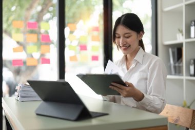 Evrak işleri. Mutlu gülümseyen Asyalı iş kadını modern ofisin ahşap masasında oturuyor ve rapor dökümanlarını okuyor..