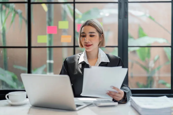 Young business woman, or company employee holding accounting bookkeeping documents checking financial data or marketing report working in office with laptop. Paperwork management.
