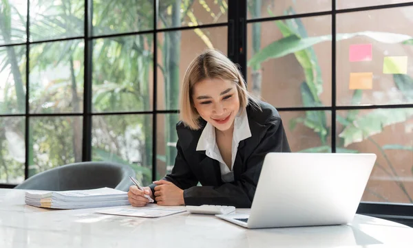 Young business woman, or company employee accounting bookkeeping documents checking financial data or marketing report working in office with laptop. Paperwork management.