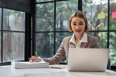 Ofisteki masada dizüstü bilgisayar ve belgeler kullanan genç iş kadınının portresi..