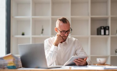 Düşünceli genç işadamı tablete bakıyor, şaşkın, kararsız görünüyor, görevleri analiz etmekten rahatsız, bir sorusu var ya da emin olamıyor..