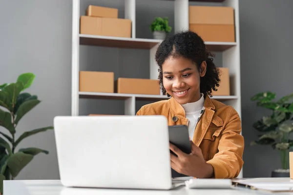 sme business idea. African Americans woman selling online at home with laptop to take orders and to deliver yellow parcel boxes online delivery ideas.