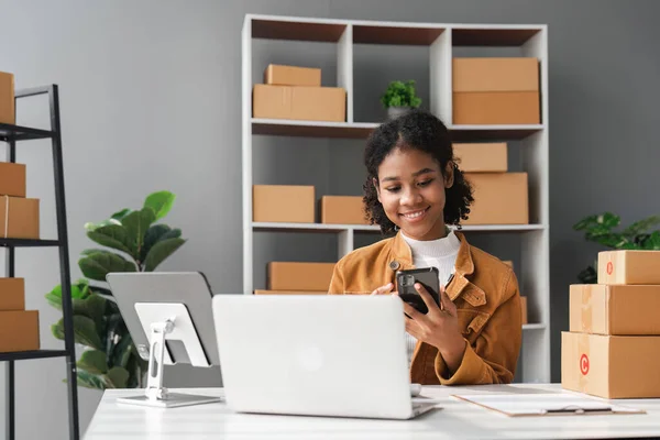 sme business idea. African Americans woman selling online at home with laptop to take orders and to deliver yellow parcel boxes online delivery ideas.