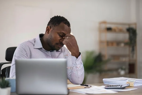 Stressed business man sitting at office workplace. Tired and overworked black man. Young african-american exhausted men in stress working on laptop computer.