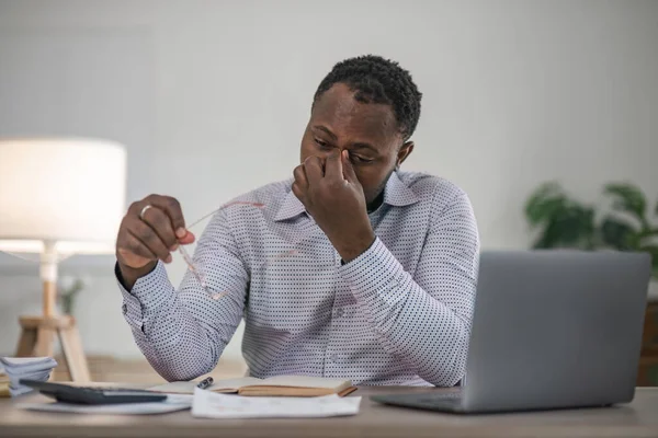 Stressed business man sitting at office workplace. Tired and overworked black man. Young african-american exhausted men in stress working on laptop computer.