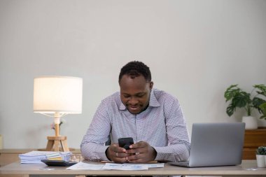 Cep telefonu kullanan bir iş adamı, dizüstü bilgisayarda çalışmakla internete bakmakla ya da ofis masasında mali verileri olan akıllı telefondan internet uygulamalarını kontrol etmekle meşgul..
