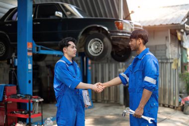 Garajda iki Asya otomotiv tamircisi tokalaşması. Mekanik atölyesinde çalışan araç servisi yöneticisi, müşteri için kontrol ve bakım otomobil motorundan sonra mutlu ve başarılı hissedin..