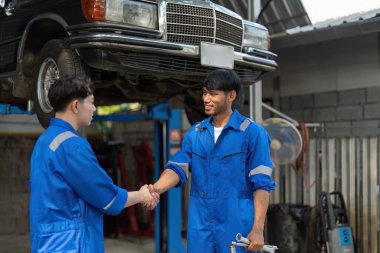 Garajda iki Asya otomotiv tamircisi tokalaşması. Mekanik atölyesinde çalışan araç servisi yöneticisi, müşteri için kontrol ve bakım otomobil motorundan sonra mutlu ve başarılı hissedin..