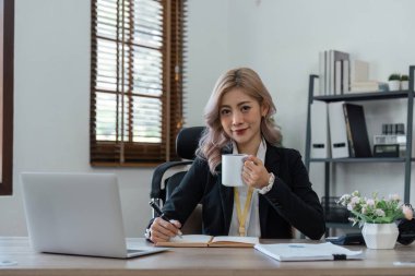 Gülümseyen genç iş kadını, bir fincan kahve içerken taşınabilir dizüstü bilgisayarda çalışıyor..