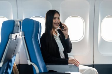 Başarılı genç iş kadını uçak kabininde otururken cep telefonuyla konuşuyor..
