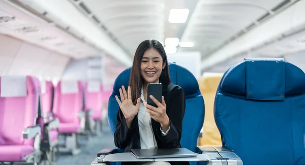 Asian female using mobile phone with talking and Video calls in airplane, Business traveling and technology concept.