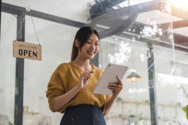 Genç bayan önlüklü bir garson, kafenin sahibi kapıda duruyor ve açık bir tabela ile müşterileri bekliyor. Küçük işletme konsepti, kafeler ve restoranlar.