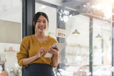Genç bayan önlüklü bir garson, kafenin sahibi kapıda duruyor ve açık bir tabela ile müşterileri bekliyor. Küçük işletme konsepti, kafeler ve restoranlar.