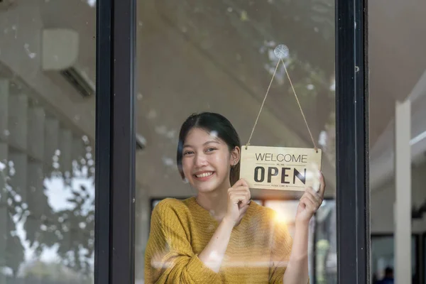 Young woman is a waitress in an apron, the owner of the cafe stands at the door with a sign Open waiting for customers. Small business concept, cafes and restaurants.