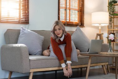 Genç, rahat, gülümseyen, güzel bir kadın evdeki kanepede rahatlıyor. Mutlu pozitif güzel bayan mutluluğun tadını çıkarıyor..