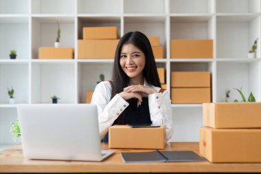 Önlüklü Asyalı genç bir iş kadını çevrimiçi paket kutusu deposunda çalışıyor ve online ürün satıyor..
