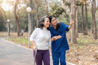 Hemşire yaşlı kadına Walker 'la yardım ediyor. Hemşire el ele tutuşuyor ve yaşlı bir kadının parkta yürümesine yardım ediyor..