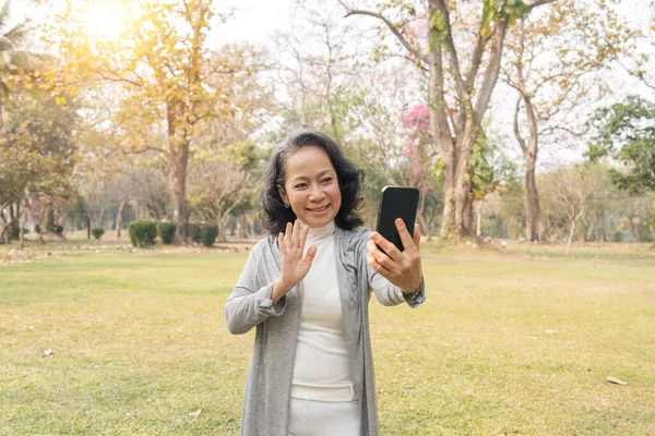 亚洲60多岁的祖母与家人或朋友在公园度假时使用手机视频通话 — 图库照片