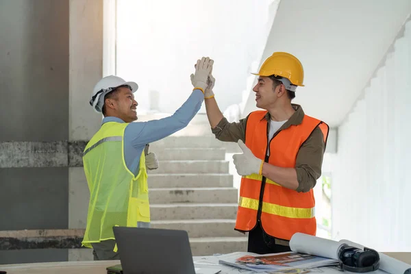 Engineer a high five to his friend colleague in the construction site, worker people celebrating their success with a high five, teamwork.