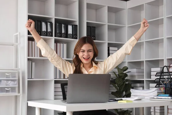 Success at work, good deal. Asian business woman looks at the laptop screen, screams excitedly and raises his fists in a victory gesture.