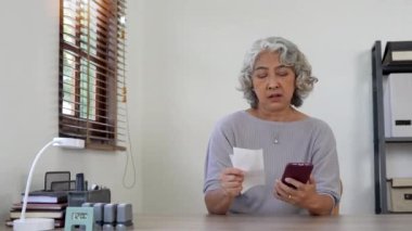 Evde akıllı bir telefonla faturaları ödeyen yaşlı bir kadın..