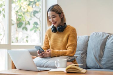 Evde akıllı telefon cihazıyla cep telefonu tutan mutlu genç kız. Yeni sosyal medya aboneliği, internetten satın alma, uygulama üzerinden ürün sipariş etme.