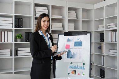 Ofis kurulunda grafik ve çizelgeleri göstererek sunumda kendine güvenen bir iş kadını.