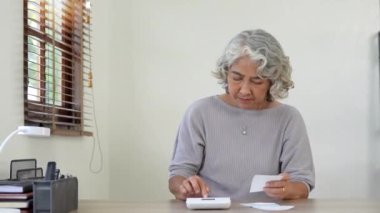 Yaşlı kadın hesaplar, yazar, faturaları internetten öder, evde çalışan mali raporları hazırlar. Odaklanmış olgun bir kadın, mali kontrol ile meşgul muhasebecilik işi yapıyor..