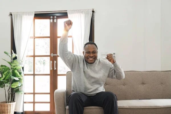 stock image Happy african american man having fun at home, screaming with remote controller in his hand, watching football game on TV, empty space. Black guy enjoying his weekend, watching TV in living room..