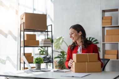 Dükkanında dizüstü bilgisayarla çalışan bir kız. Genç bir kadın, müşteriye göndermek için bir paket kutusu hazırlıyor. e-ticaret çevrimiçi satışlar.