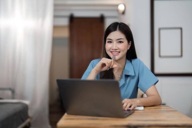 Asyalı güzel bir kadın dizüstü bilgisayarla rahatlarken masa başında yaratıcı bir kadın çalışıyor ve klavyede daktilo kullanıyor. Ev konseptinde çalışıyor..