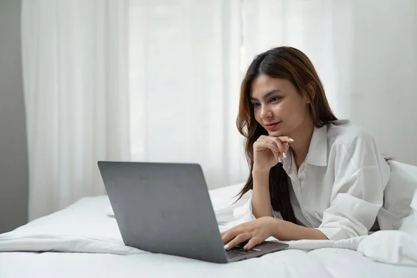 若い女性がリラックスし ソーシャルアプリをチェックし 寝室を作業する上でラップトップコンピュータを使用して — ストック写真