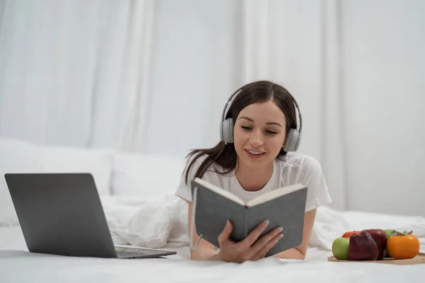 リラックスした女性は本を読んで 休日のためのあなたのラップトップの音楽と朝の果物を聞く — ストック写真