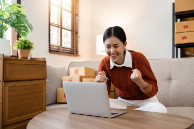 Mutlu küçük işletme sahibi, en yüksek satışlarını kutluyor. Evdeki dizüstü bilgisayarında heyecanla ellerini kaldırıyor..