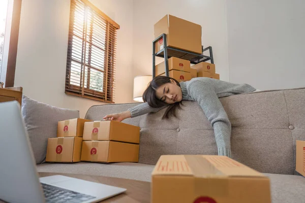 Tired Young Asian woman working and sleep at couch with packing box feels exhaustion having day nap lack of energy. Overwork load packing box.