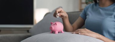 Kadın elleri pembe bir kumbara tutuyor ve oraya para koyuyor. Tasarruf, tasarruf, yatırım kavramı.