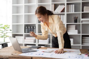 Evdeki çalışma masasında oturan bir kadın dizüstü bilgisayara bakıyor, yumruk tokuşturuyor, başarıyı kutluyor, mutlu ve heyecanlı hissediyor. İş kadını iş projesini bitirdi ya da anlaşma onaylandı.
