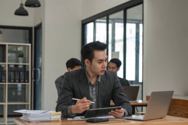 İşadamı ofisinde oturuyor ve dizüstü bilgisayar ve tablet üzerinde çalışıyor..