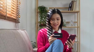 Banka kartı tutan mutlu kadın, cep telefonu internet alışveriş uygulamasına CVV kodu ya da ödeme bilgisi giriyor.