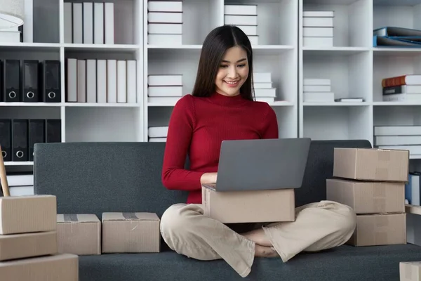 Female seller write the customers address on the parcel box to prepare for delivery and using laptop checking days sales on the online store, Concept of parcel delivery and selling online.