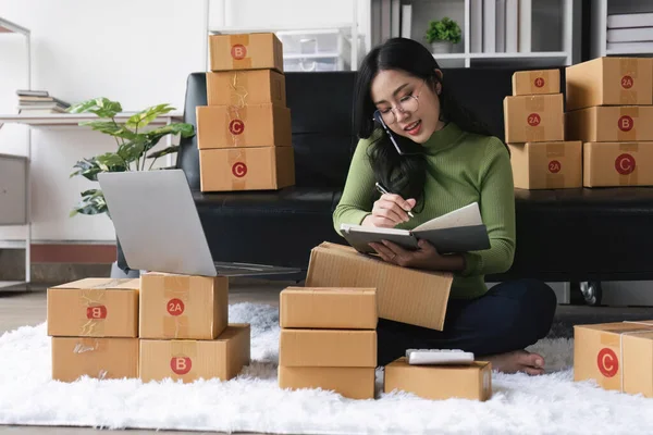 Female small business owner using laptop checking parcel box. Older entrepreneur seller preparing retail package postal shipping order at home.