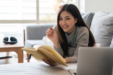 Çekici genç Asyalı kadın en az ve rahat oturma odasında uyur kitap okumaktan zevk alır..