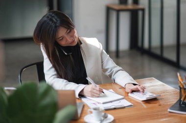 İş kadını ya da muhasebeci not alıyor ve not defterinde not alınırken iş verilerini hesaplamak için hesap makinesi ve dizüstü bilgisayar üzerinde çalışıyor...