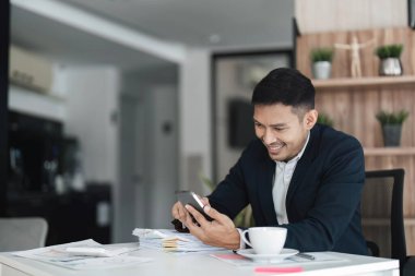 Asyalı iş adamı ofisinde akıllı telefon kullanıyor...