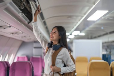 Kadınlar uçakla seyahat eder. Güç yolcusu el bagajını uçak koltuklarının üstündeki dolaplara koyuyor..