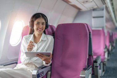 Uçakta birinci sınıfta pencere kenarında oturan Asyalı genç kadın uçuş, seyahat ve iş konsepti.